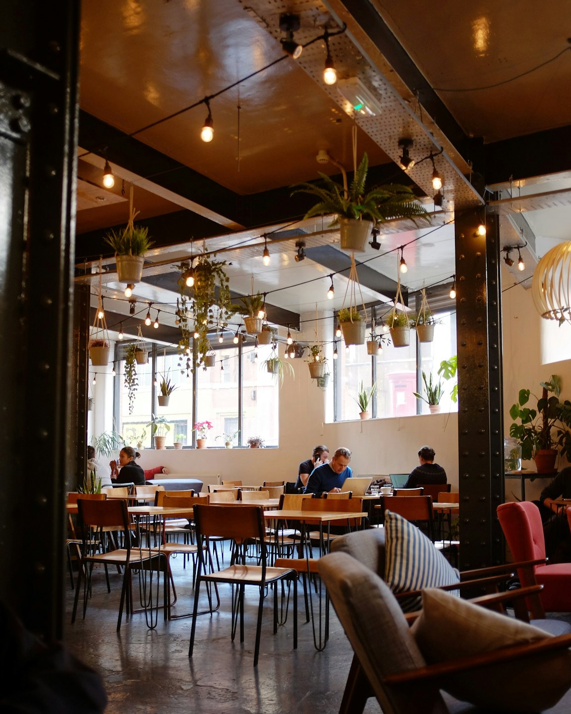 Gente trabajando en mesas en una cafetería luminosa de coworking con plantas.