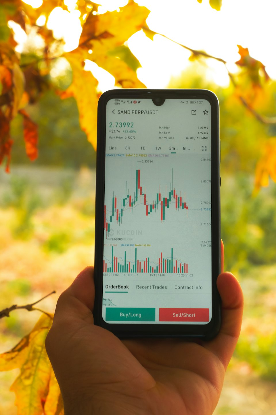 Mano sostiene un teléfono que muestra una aplicación de comercio de criptomonedas con gráficos.